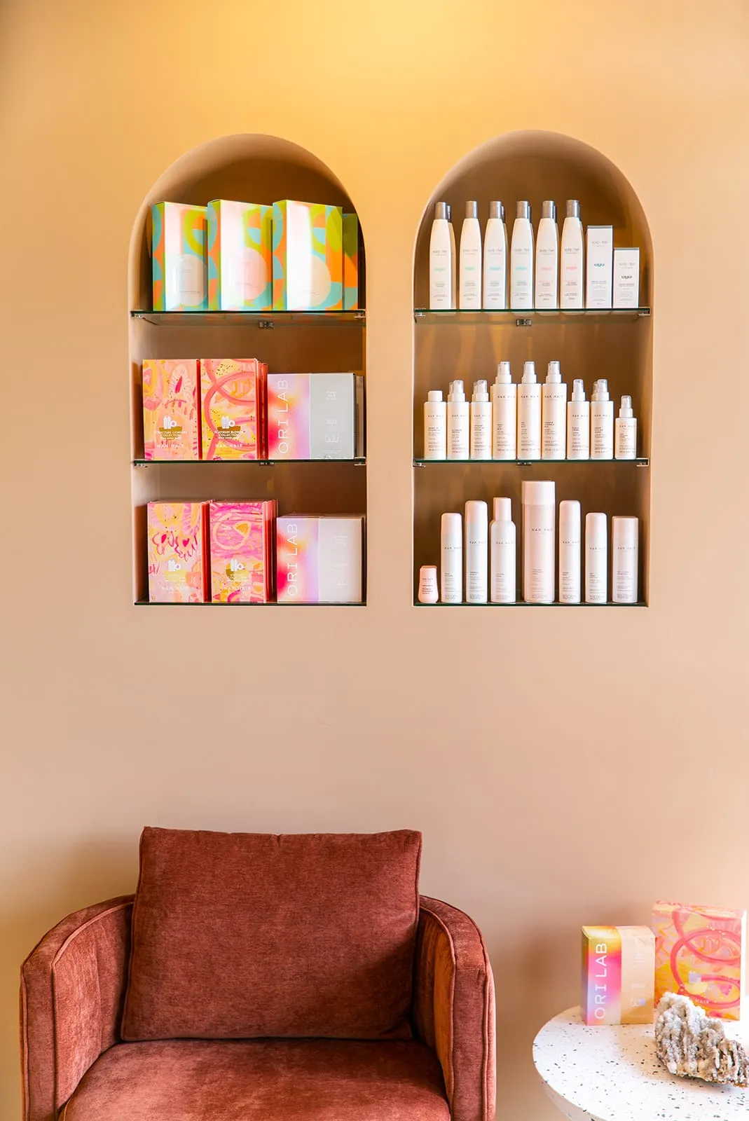 Arched product shelving above a terracotta armchair at Hair By Rena, Gregory Hills